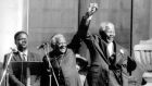 In Cape Town, Desmond Tutu joins hands with Nelson Mandela in   triumph after the latter was proclaimed president of South Africa in 1994.   