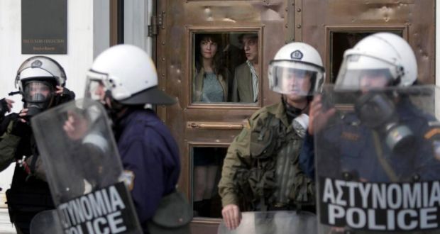  Tourists look out from behind the door of  a hotel in  Athens during a demonstration remembering  the victims of a 1973 uprising against the military junta last month. Photograph: Yannis Kolesidis/Epa