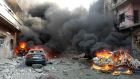 Flames rise from damaged cars where bombs exploded on a commercial street in Homs province. Photograph: AP Photo/SANA