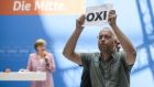 A protester holds a sheet with the Greek word for ‘No’ during an open house presentation of Germany’s conservative Christian Democratic Union (CDU) party  in Berlin, while German chancellor Angela Merkel speaks in the background. Photograph: Getty Images
