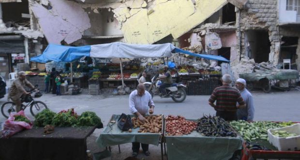 Civilians shop for vegetables and fruits displayed in front of a damaged building in Aleppo’s Bustan al-Qasr neighborhood, Syria. Photograph: REUTERS/Hosam Katan 