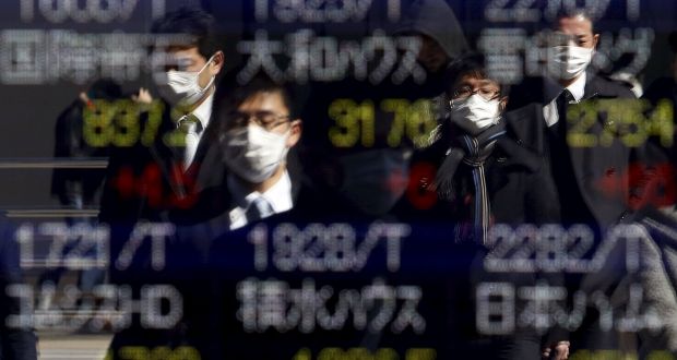 Pedestrians wearing masks are reflected in an electronic board showing various stock prices outside a brokerage in Tokyo, Japan. Photograph: Yuya Shino/Reuters