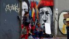 A street vendor sits next to graffiti depicting Venezuela’s late President Hugo Chavez in Caracas. Photograph: Mariana Bazo/Reuters