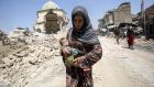 An Iraqi woman, carrying an infant, walks by the destroyed al-Nuri Mosque as she flees from the Old City of Mosul on July 5, 2017. Photograph: Ahmad Al-Rubaye/AFP/Getty 