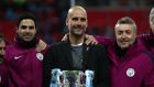 Pep Guardiola and his assistants Mikel Arteta and Domenec Torren with the League Cup trophy. His yellow ribbon is visible beneath his blazer. Photograph: Catherine Ivill/Getty Images