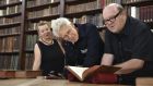 Adam Clayton of U2 and the band’s former manager, Paul McGuinness look at an English-Irish dictionary dating from 1768 as Irish College director Nora Hickey M’sichili looks on.