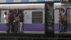 Passengers stand on the side of train carriages in Mumbai. Photograph: Dhiraj Singh/Bloomberg via Getty Images