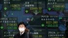 A man stands in front of an electronic stock board showing Japan’s Nikkei 225 index and other city’s index at a securities firm in Tokyo  