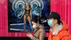 People wearing protective masks walk past a poster outside a shopping mall in Beijing, China, on Friday. Daily life in the city is affected by the Covid-19 coronavirus outbreak, with few people visiting shopping areas and stores. Photograph: Wu Hong/EPA