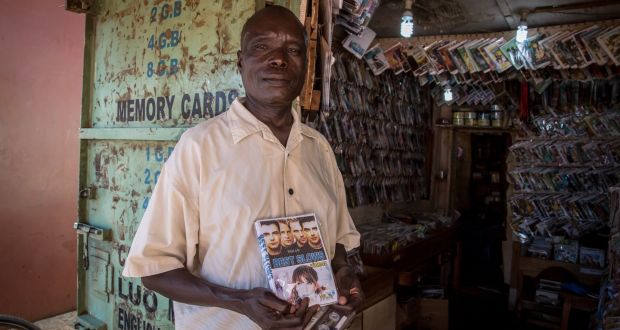 Felix Lutalo stands outside his music store in the bus park in Gulu, northern Uganda, holding a Westlife compilation he’s selling. Photograph: Sally Hayden.
