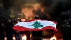  An anti-government protester carries a national flag as other burn tyres   during a protest against the power cuts, the high cost of living, the low purchasing power of the Lebanese pound at Bchara Khoury  in Beirut, Lebanon. Photograph: Wael Hamzeh/EPA 