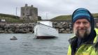 Clare Island whiskey maker Carl O’Grady and The Dolphin, the island’s former ferry and now a whiskey maturing vessel, overlooked by Grace O’Malley’s Castle. Photograph: Peter Murtagh/The Irish Times