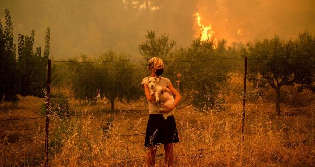 A woman holds a dog in her arms as forest fires approach the village of Pefki on Evia island, Greece’s second-largest island. Photograph: Angelos Tzortzinis / AFP via Getty 