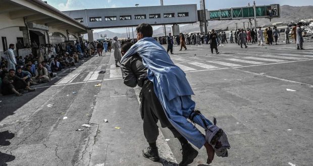 A volunteer carries an injured man as other people can be seen waiting at the Kabul airport in Kabul. Photograph: Wakil Kohsar / AFP / Getty Images