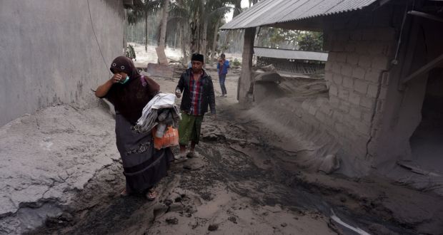 Villagers carry their belongings near a damaged house covered by volcanic ash from the Mount Semeru eruption in Lumajang, East Java. Photograph: Ammar/EPA