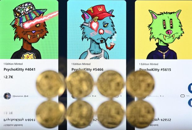 Gold-plated souvenir cryptocurrency coins arranged beside a screen displaying a Crypto.com NFT marketplace, showing three PsychoKitty NFTs created by psychedelic artist Ugonzo. Photograph: Justin Tallis/AFP via Getty