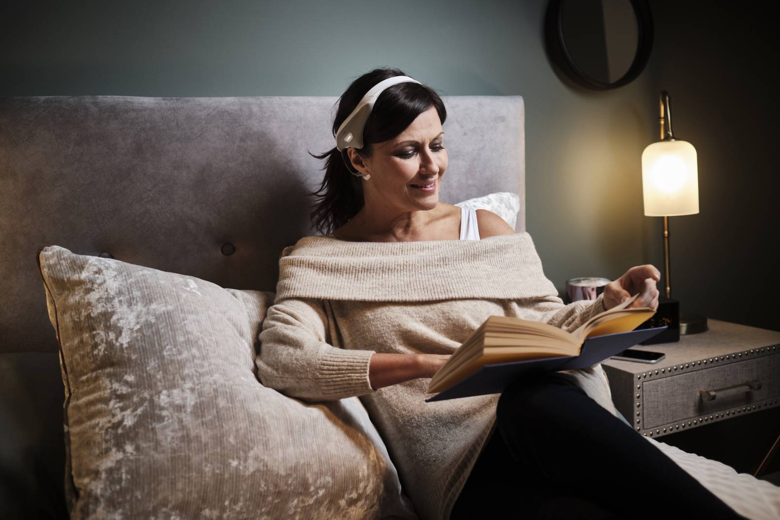 Woman lying on a bed reading while wearing the modius band on her head.