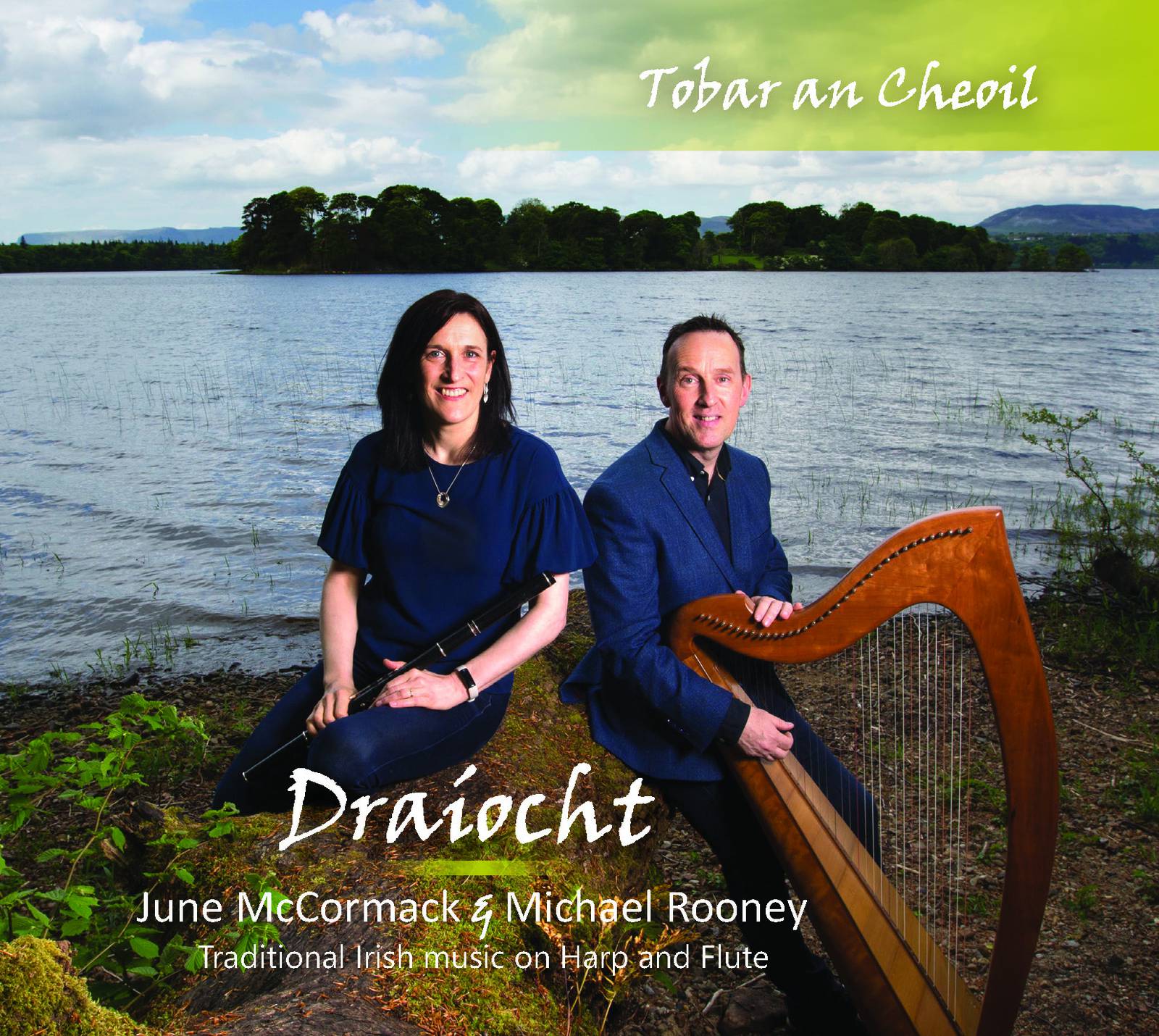 June McCormack holds her flute beside Michael Rooney with his harp, both sitting beside a lake