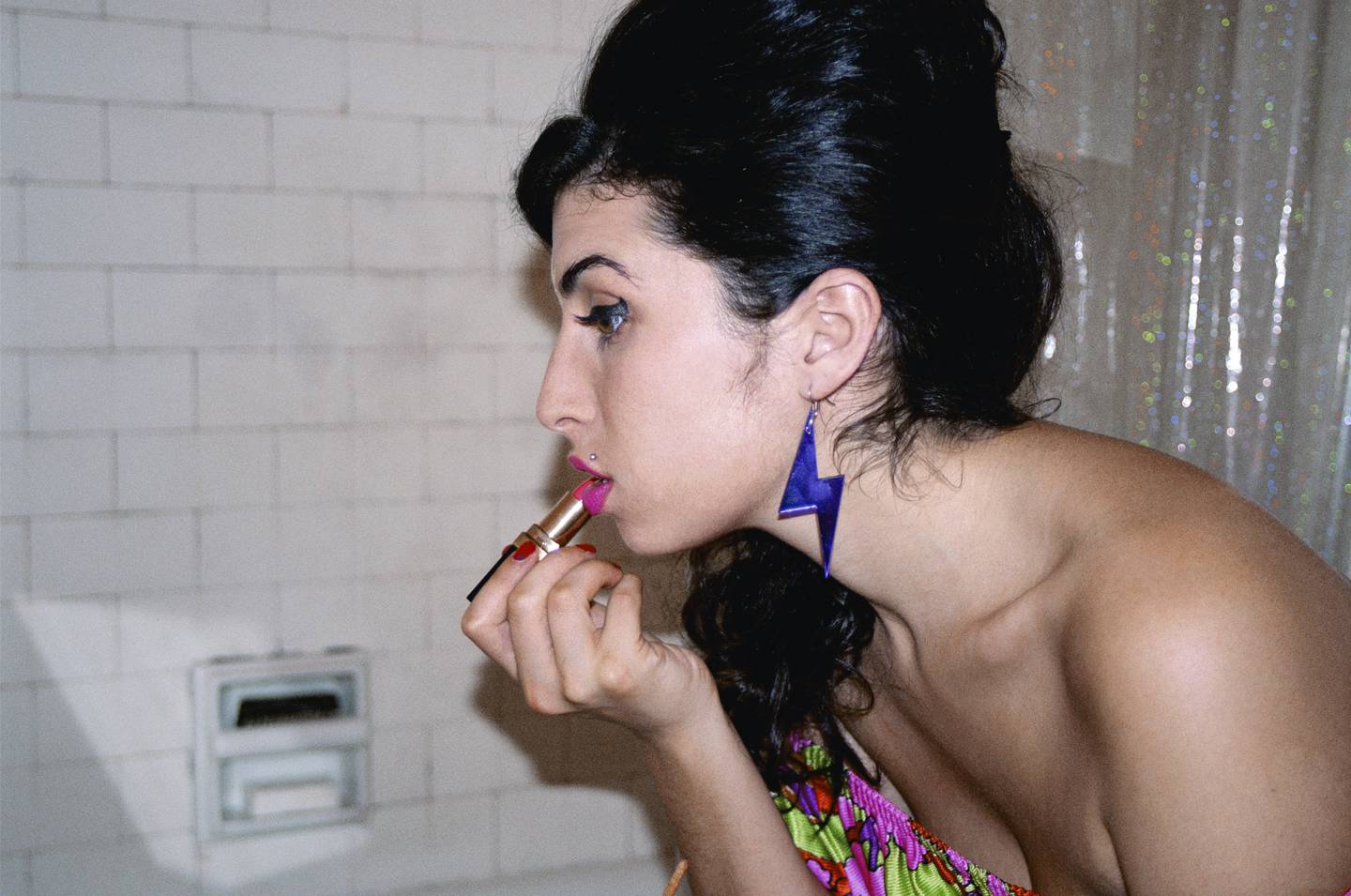 Amy Winehouse wearing purple thunderbolt earrings and applying pink lipstick in a New York bathroom, is now part of the National Portrait Gallery collection in London.