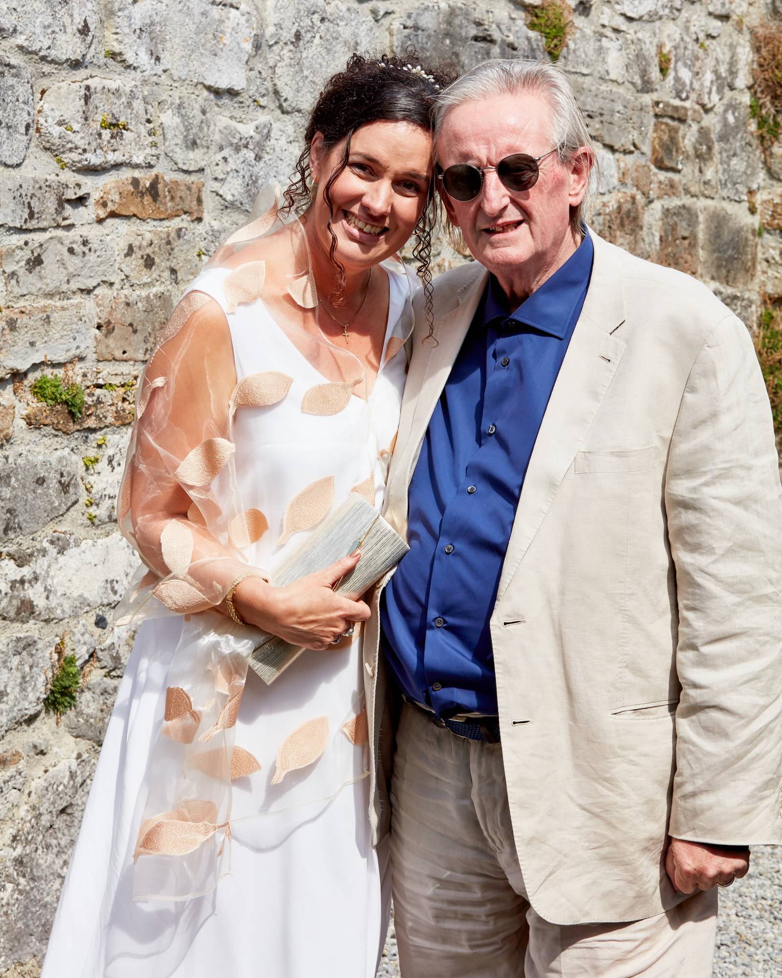 L-R: Helen Phelan in white wedding dress beside Micheál Ó Suilleabháin in cream coloured suit and blue shirt. Both standing.