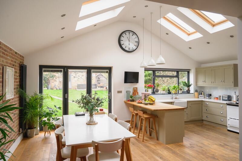 Unoccupied kitchen, dining table seating six, brick wall, hardwood floor, wall clock, skylight, and access to backyard.