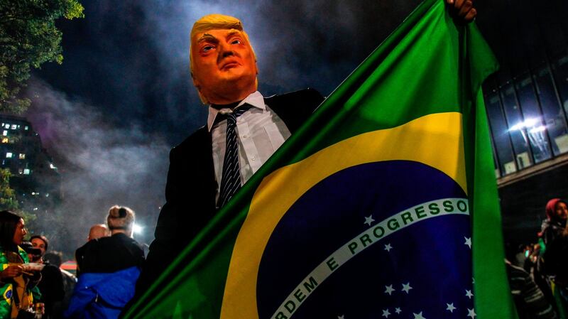 A Bolsonaro supporter wears a mask of US president Donald Trump as he celebrates after Bolsonaro won. Photograph:  Miguel Schincariol/AFP/Getty Images