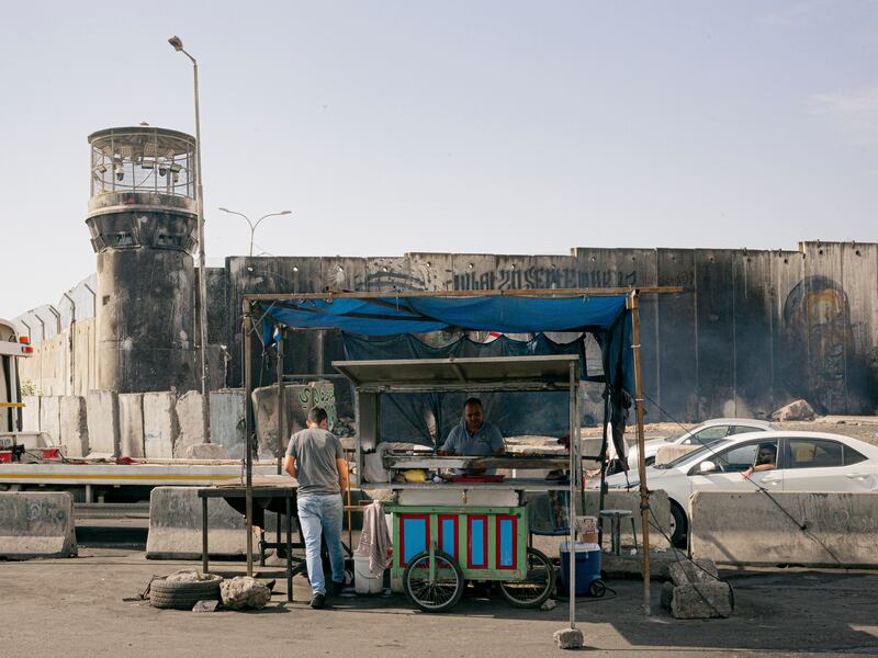 A vendor near a checkpoint where Palestinians sometimes wait all day trying to cross in Qalandia, West Bank. Photograph: William Keo/The New York Times
                      