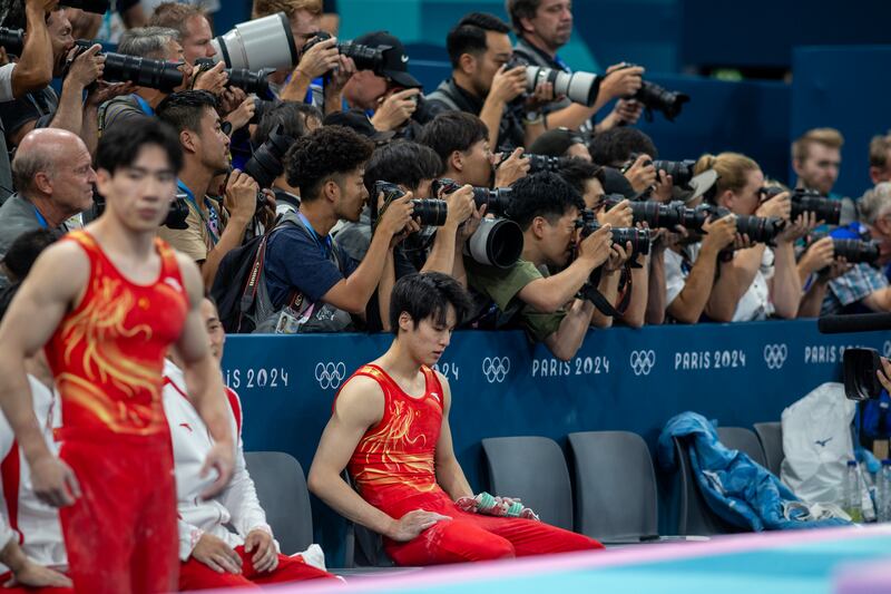Photographers concentrate on the gold medal-winning Japanese team as Su Weide of China sits dejected after his two falls on the horizontal bar helped tip the contest. Photograph: Tim Clayton/Corbis via Getty Images
