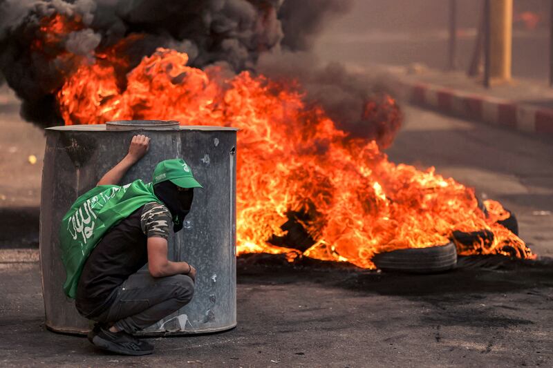 A masked Palestinian protester takes cover during clashes with Israeli forces following a rally in solidarity with Gaza by supporters of Fatah and Hamas in the city of Hebron in the occupied West Bank on Friday. Photograph: Hazem Bader/AFP