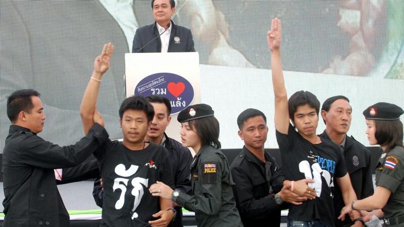 Two students  were arrested by police officers and security guards as they flashed anti-coup sign in front of Prime Minister Prayut Chan-o-cha (back) while delivering a speech during his visit in Khon Kaen province, north eastern Thailand, yesterday. Photograph: EPA