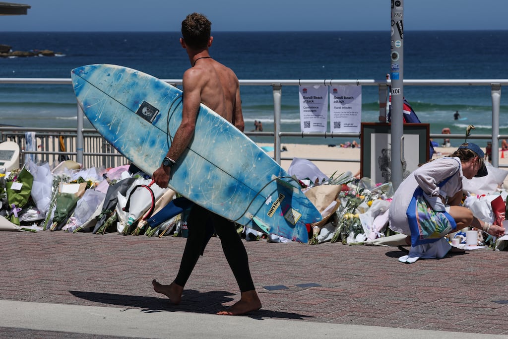A surfer walks past floral tributes left at the promenade of Bondi Beach in Sydney on December 18, 2025, to honour victims of the shooting that took place there on December 14. The attack at Bondi Beach on December 14 was one of the deadliest in Australian history. (Photo by DAVID GRAY / AFP via Getty Images)
