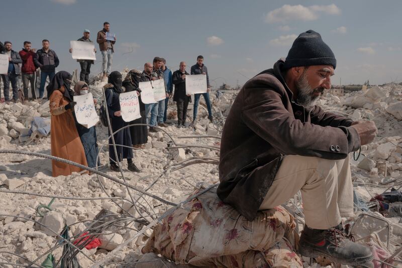 Syrians protest against lack of international aid while a man sits on the rubble of his home in the town of al-Atarib, Aleppo province, Syria. Photograph: Emily Garthwaite/The New York Times