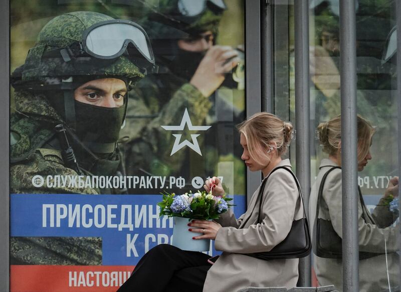 A Russian woman sits on a bus stop in front of poster advertising military conscription showing Russian soldiers in Moscow, Russia. Photograph: Yuri Kochetkov/EPA
