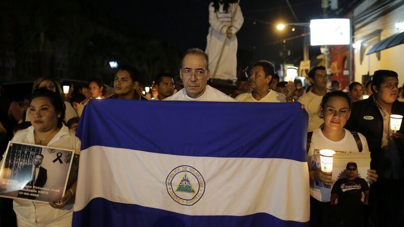 Fr Edwin Roman  holds a Nicaraguan flag next to people holding photos of relatives who died in  protests during the procession of El Silencio on Holy Thursday  in Masaya. Photograph:  Inti Ocon/ AFP/ Getty Images