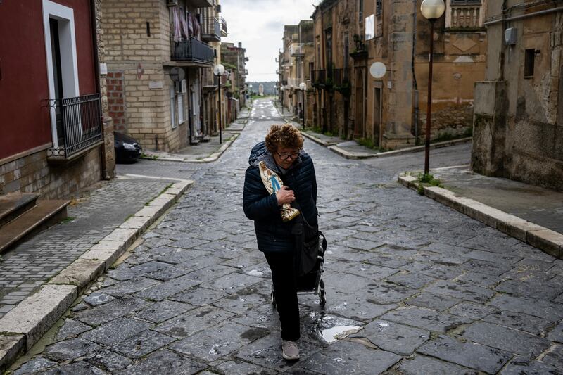 A woman holds a statue of the Virgin Mary as she leaves her home after returning with firefighters to collect her belongings in Niscemi, Sicily. Photograph: MARCO BERTORELLO / AFP via Getty Images
