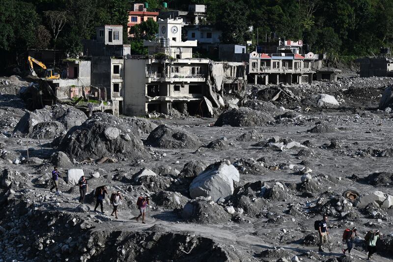 In late September, people walk past masses of silt and sediment near destroyed homes in the aftermath of the August 26th flash flood at Betrawati Bazaar, in Nepal's Rasuwa district. Photograph: Prakash Mathema/AFP/Getty