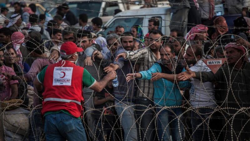 A Turkish Red Crescent worker hands water through the wire to Syrian Kurds waiting to be allowed to enter Yumurtalik, Turkey. Photograph: New York Times