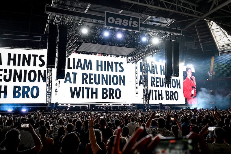 Oasis: Giant screens show press coverage teasing of the band's possible reunion at the back of the stage on the opening night of their Live ’25 Tour at Principality Stadium in Cardiff. Photograph: Gareth Cattermole/Getty Images
