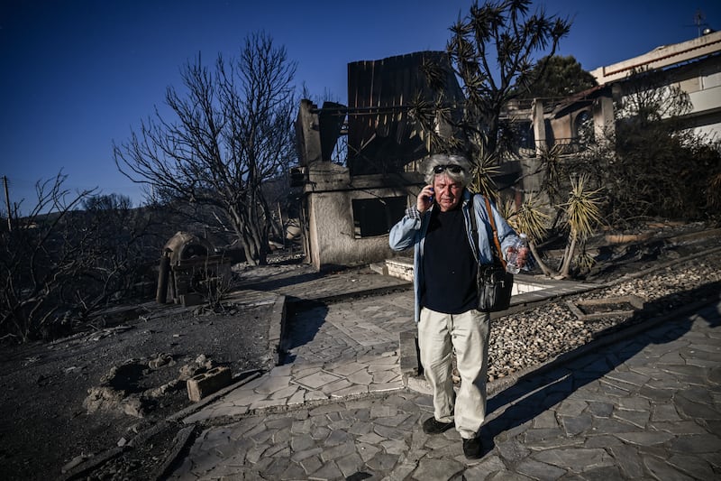 A man talks on his phone as he stands next to a burnt house following a wildfire in Thymari, southeast of Athens. Photograph: ARIS MESSINIS/AFP via Getty Images
