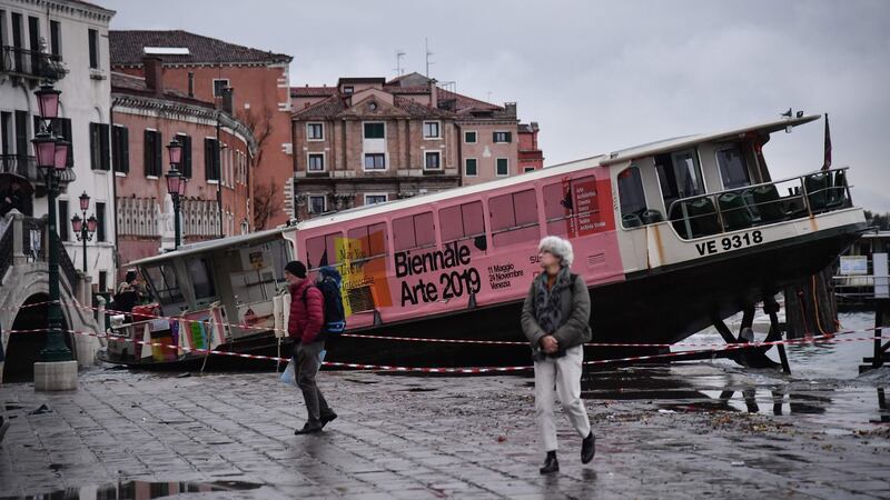 People walk past a stranded taxi boat on Riva degli Schiavoni in Venice on Wednesday after an exceptional overnight high tide of 187cm was recorded in the Italian lagoon city. Photograph: Marco Bertorello/AFP via Getty Images.