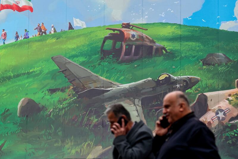 Iranian men speaking on their mobile phones walk past an anti-US billboard displayed on a building in Tehran's Valiasr Square. Photograph: Atta Kenare/AFP/Getty Images
