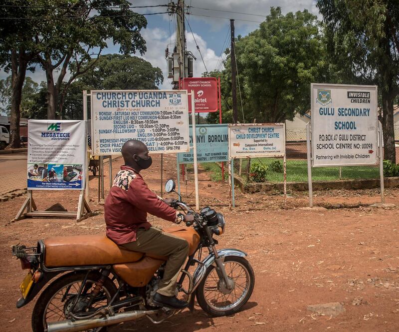 A boda boda driver rides past a sign for Gulu secondary school, which has been supported by the charity Invisible Children, producer of the Kony 2012 video