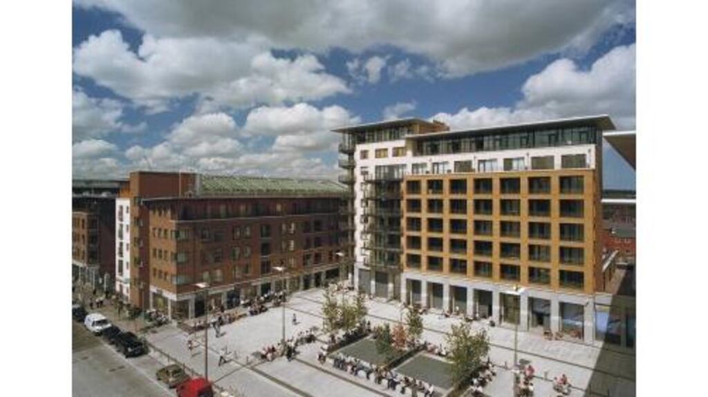 Summertime view of Mayor Square in Dublin's Docklands showing new apartment blocks with ground-floor retail units, designed by Anthony Reddy and Associates