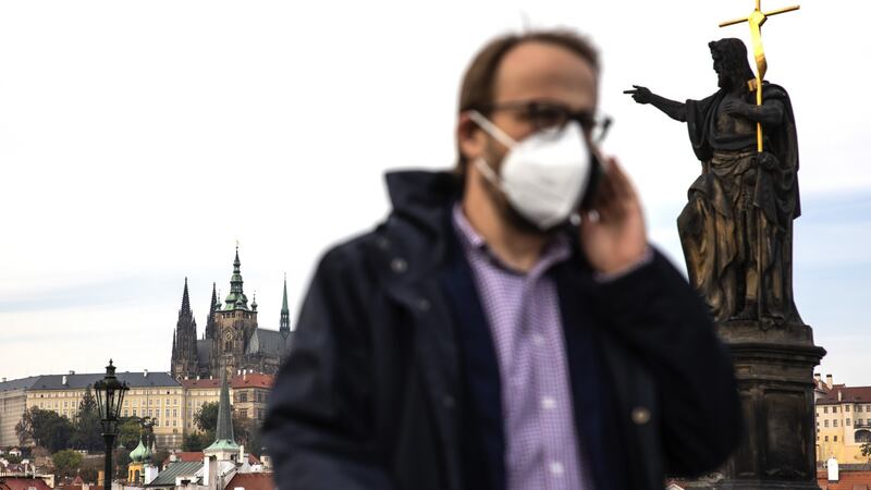 A pedestrian wearing a protective face mask passes a statue on the Charles Bridge in Prague, Czech Republic. Photographer: Milan Jaros/Bloomberg