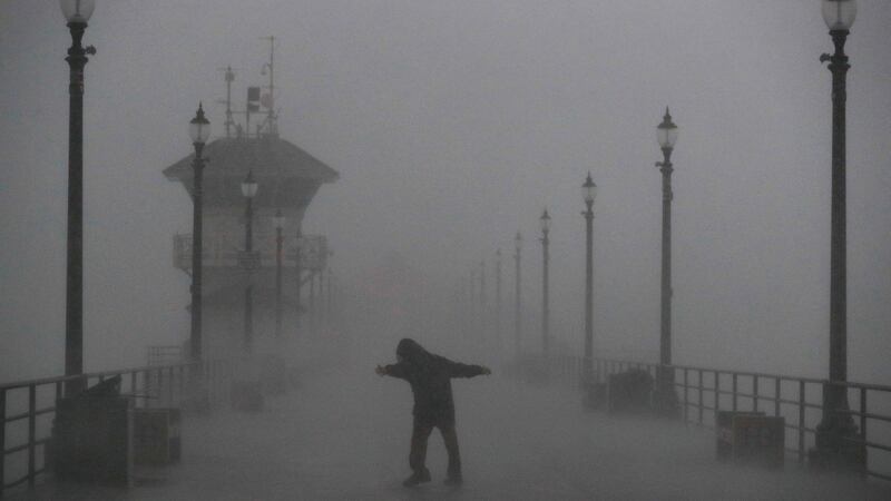 A man struggles against gusty wind and heavy rain as he walks along a pier  in Huntington Beach, California on Friday. Photograph: AP