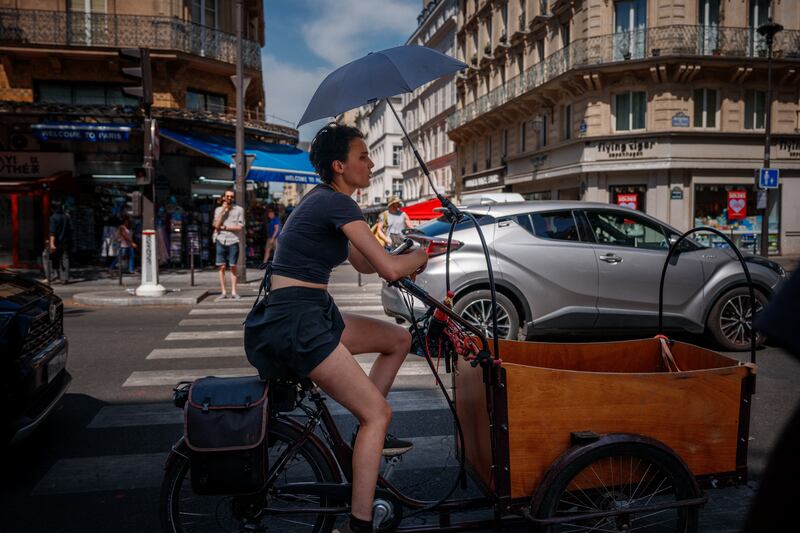 A woman protects herself from the sun under an umbrella as she rides a bicycle in Paris on June 25th. Photo: Dimitar Dilkoff/AFP via Getty Images