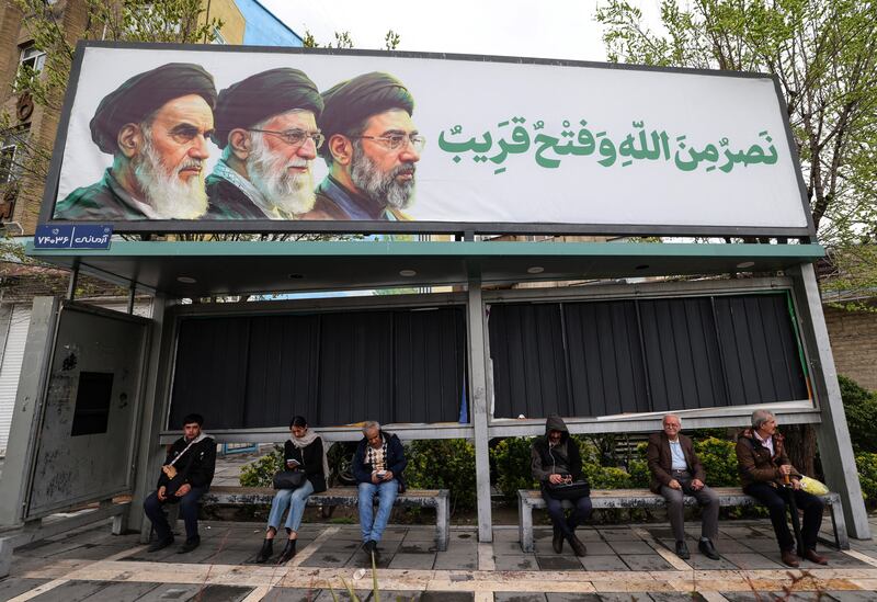 Iranians sit at bus stop beneath a billboard depicting Iran's late supreme leader Ayatollah Ruhollah Khomeini, his successor the late Ayatollah Ali Khamenei and the new supreme leader Mojtaba Khamenei in Tehran on Tuesday. Photograph: Atta Kenare/AFP via Getty Images
