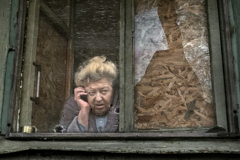 Yelizaveta Dragunova (75) talks on her phone from her damaged window as she observes food distribution in the Ukrainian city of Kherson, where drones have killed 200 people and injured about 2,000 in the last year, authorities say. Photograph: Mauricio Lima/The New York Times