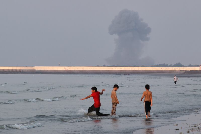 Three boys play in the shallow waters of the Strait of Hormuz, as a plume of smoke rises from an explosion in the background. Photograph: Razieh Poudat/AP