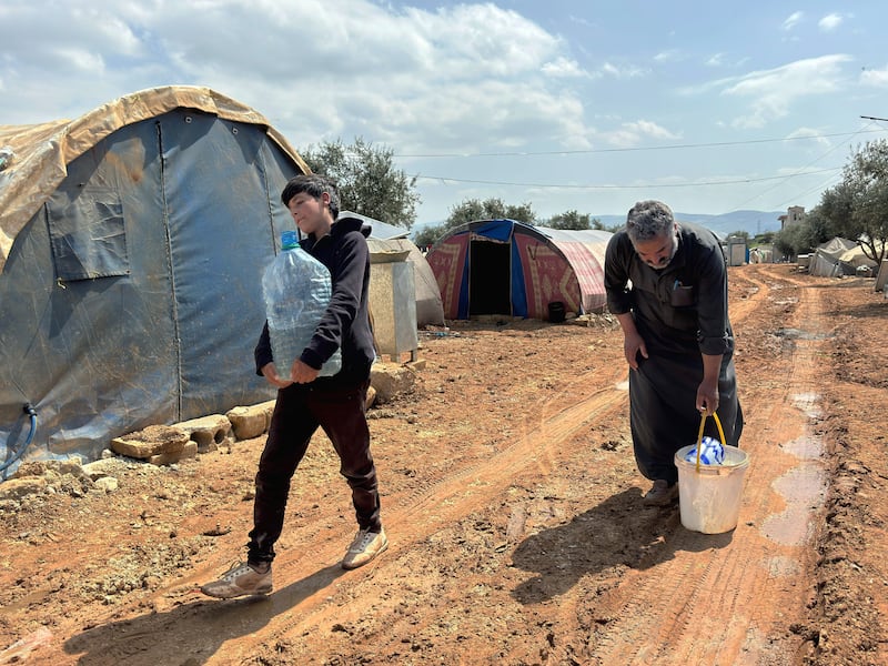 Hussein and his 12 year old son Mudar carry water to their family tent across muddy roads